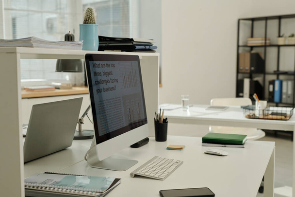 Lugar de trabajo del trabajador de cuello blanco con monitor de computadora, teclado, cuaderno, documentos financieros, teléfono inteligente y ratón en el escritorio - Foto, Imagen
