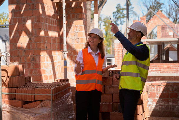 Woman real estate agent surprised with building construction speed, talking to foreman spending time on construction site - Photo, Image