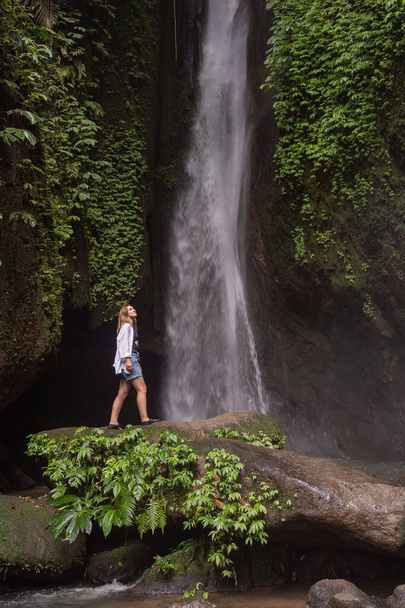 Waterfall in tropical jungle and alone woman tourist. Leke Leke waterfall in Bali, Indonesia. - Zdjęcie, obraz