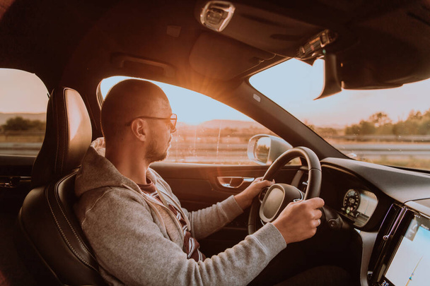 A man with a sunglasses driving a car at sunset. The concept of car travel.  - Foto, immagini