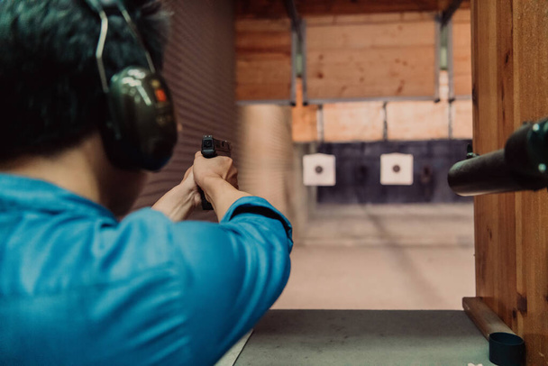 A man practices shooting a pistol in a shooting range while wearing protective headphones.  - Fotografie, Obrázek