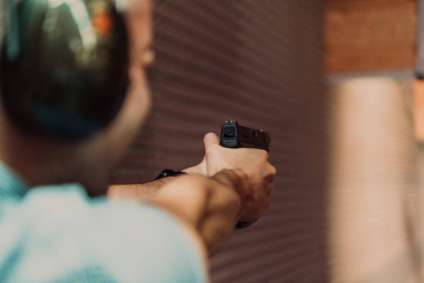 A man practices shooting a pistol in a shooting range while wearing protective headphones.  - Foto, afbeelding