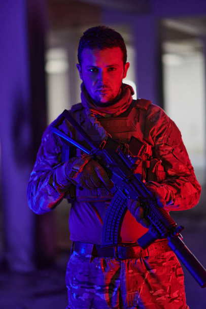 Egy hivatásos katona veszélyes küldetést hajt végre egy elhagyatott épületben, amit neonkék és lila fények világítanak meg..  - Fotó, kép