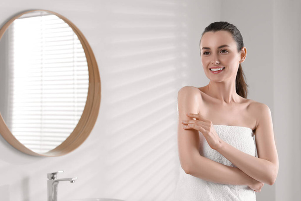 Happy woman applying body oil onto arm in bathroom, space for text - Фото, зображення