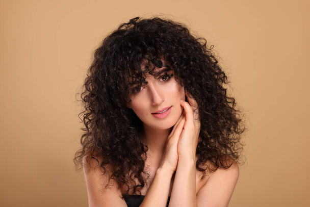 Beautiful young woman with long curly hair on beige background - Φωτογραφία, εικόνα