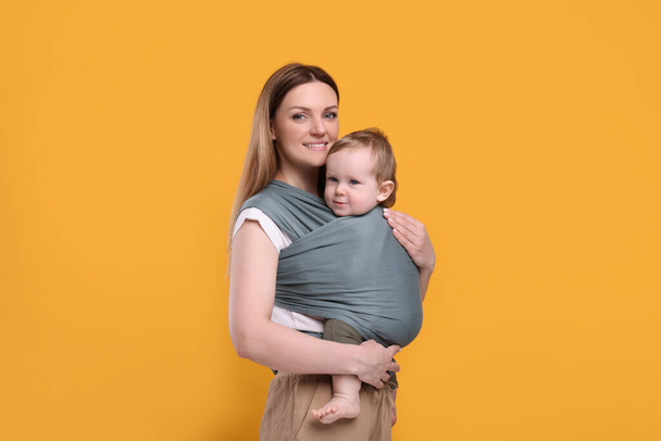Mother holding her child in baby wrap on orange background - 写真・画像