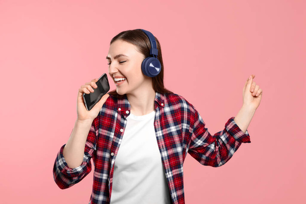 Happy woman in headphones enjoying music and dancing with smartphone on pink background - Фото, изображение