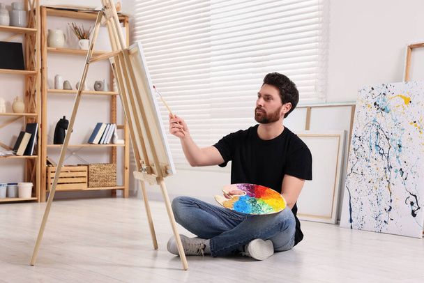Man painting in studio. Using easel to hold canvas - Foto, Imagem