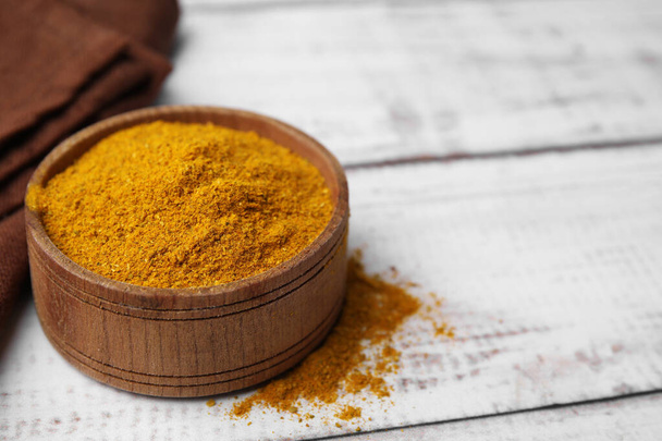 Bowl with curry powder on white wooden table, closeup. Space for text - Foto, imagen