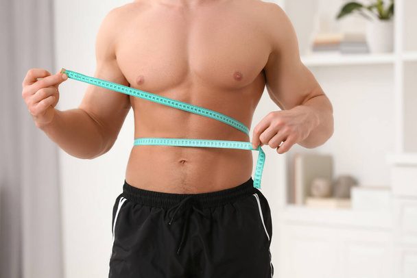Athletic man measuring waist with tape at home, closeup. Weight loss concept - Foto, immagini