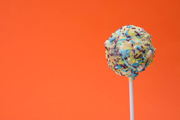 Delicious confectionery. Sweet cake pop decorated with sprinkles on orange background, closeup. Space for text - Zdjęcie, obraz