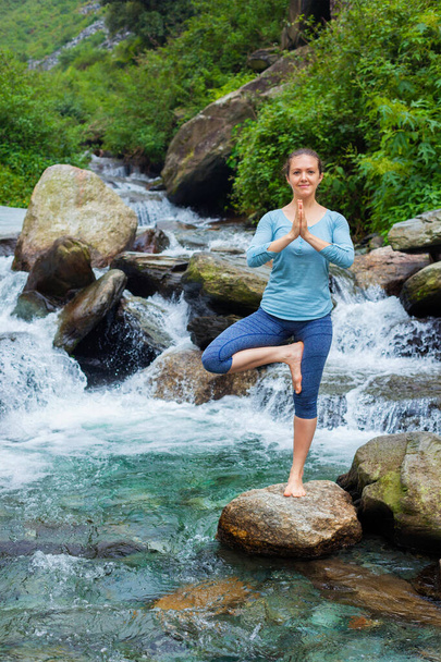 Mulher em Hatha ioga equilíbrio ioga asana Vrikshasana árvore pose em cachoeira ao ar livre
 - Foto, Imagem