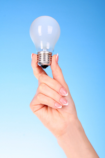 Hand mit Glühbirne auf blauem Hintergrund - Foto, Bild