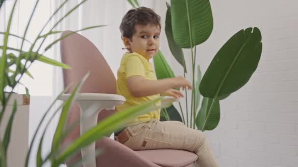 Kleine jongen ontspannen op comfortabele modieuze roterende stoel in de voorkant van laptop computer na het nemen van online lessen - Video