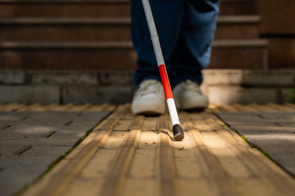 A blind woman walks outdoors using a cane along a tactile yellow tile - Foto, imagen