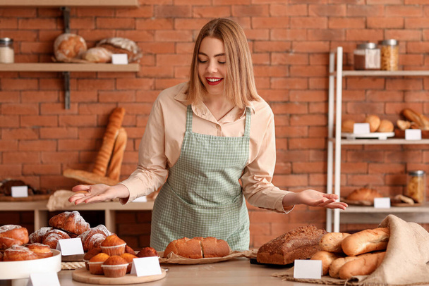 Female baker near table with fresh pastries in kitchen - Foto, afbeelding