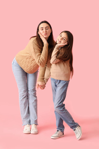 Little girl and her mother in knitted sweaters holding hands on pink background - Фото, изображение