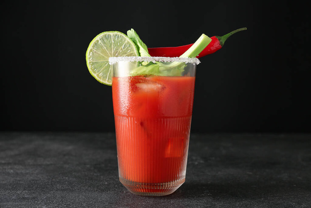 Glass of bloody mary cocktail garnished with cilantro, lime and red chili pepper on dark background - Photo, Image