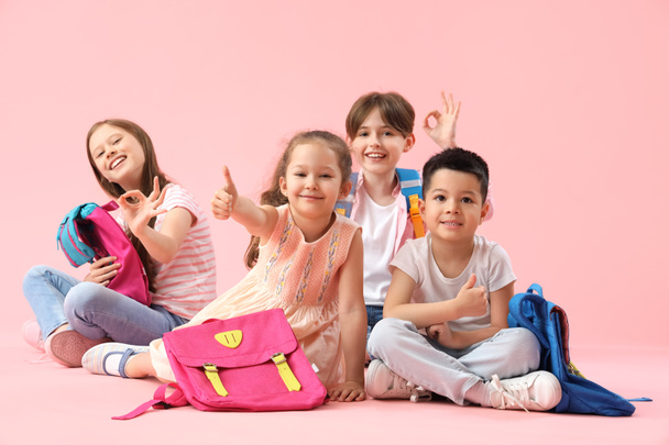 Kleine leerlingen met rugzakken met duimen omhoog op roze achtergrond - Foto, afbeelding