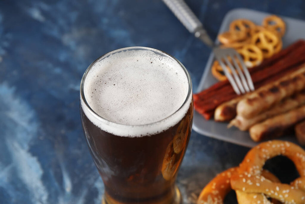 Glas koud bier en verschillende snacks op blauwe achtergrond. Oktoberfeest viering - Foto, afbeelding