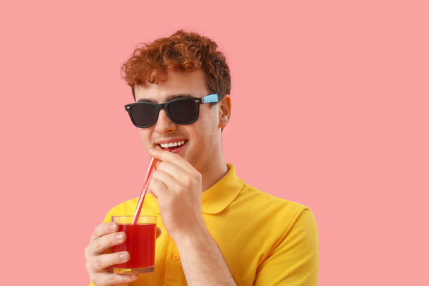 Fiatal férfi iszik piros lé rózsaszín háttér, közelkép - Fotó, kép