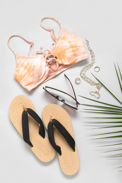 Top de bikini con estilo, chanclas, gafas de sol, accesorios y hojas de palma sobre fondo claro - Foto, Imagen