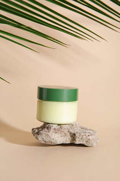 Jar of cosmetic product, stone and palm leaf on color background - Foto, imagen