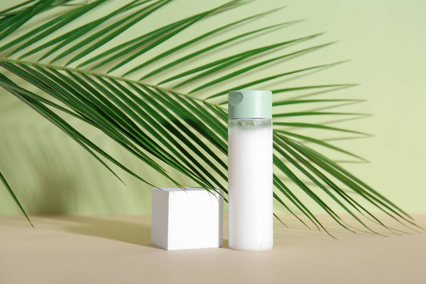 Bottiglia di prodotto cosmetico, podio in gesso e foglia di palma su fondo verde - Foto, immagini