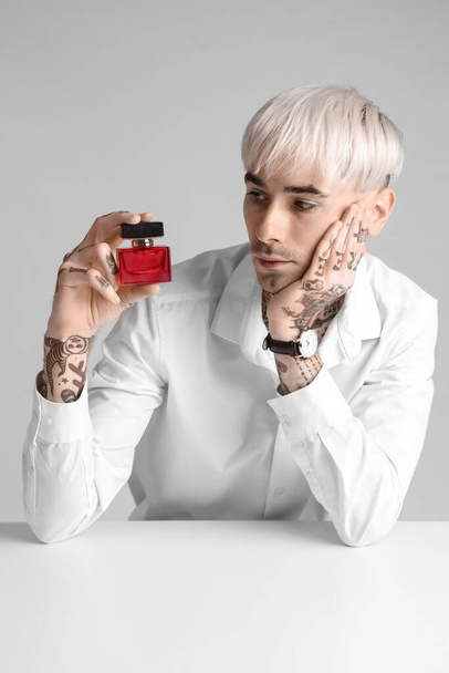 Tattooed young man with perfume at table on light background - Foto, imagen