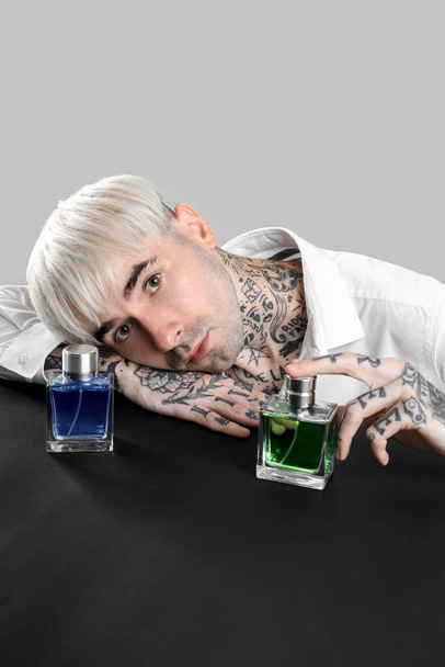 Tatuato giovane uomo con bottiglie di profumo a tavola su sfondo chiaro - Foto, immagini