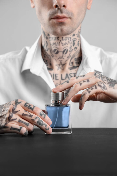 Tattooed young man with perfume at table on light background, closeup - Foto, imagen
