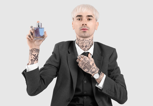 Tattooed young man in suit with perfume on light background - Foto, afbeelding
