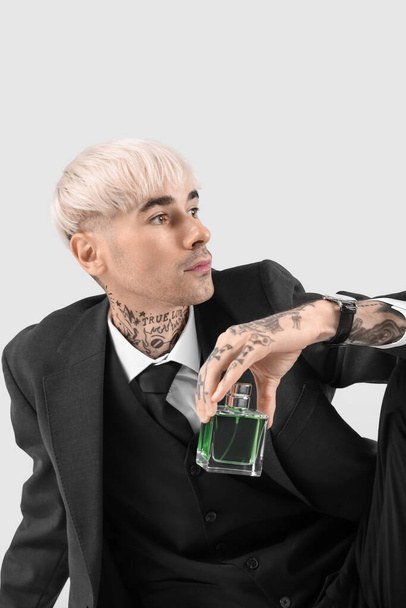 Tattooed young man in suit with perfume on light background, closeup - Photo, Image