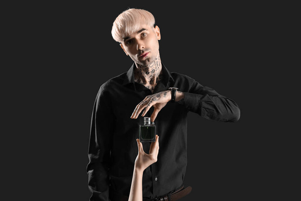 Tätowierter junger Mann und weibliche Hand mit Parfüm auf dunklem Hintergrund - Foto, Bild