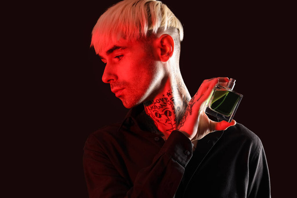 Tattooed young man with perfume on dark background, closeup - Foto, imagen