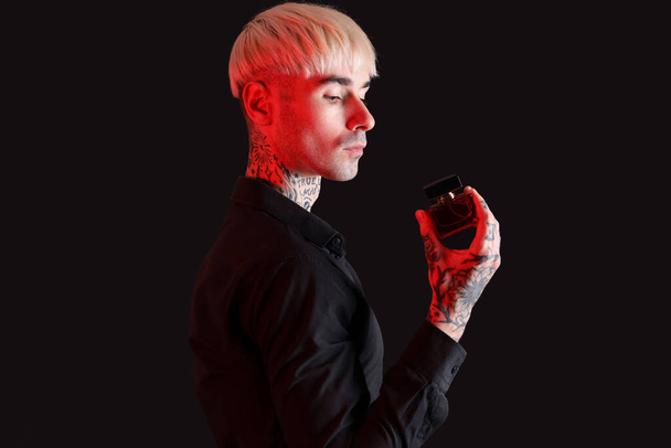 Tätowierter junger Mann mit Parfüm auf dunklem Hintergrund - Foto, Bild