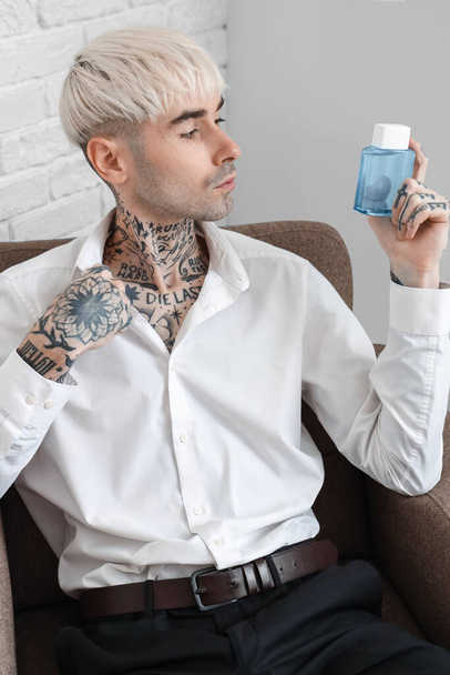 Tetovaný mladý muž s parfémem sedí v křesle doma - Fotografie, Obrázek