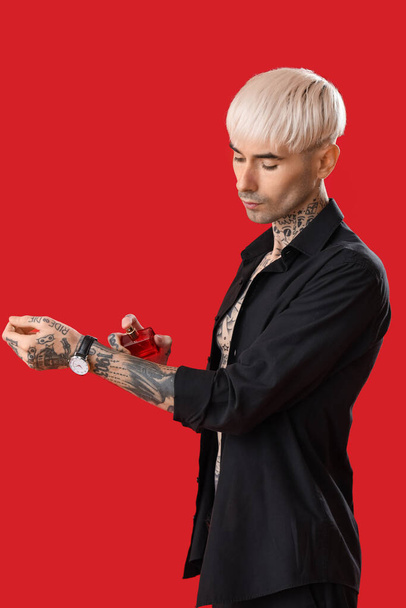Tatuado jovem homem pulverizando perfume no fundo vermelho - Foto, Imagem