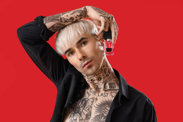 Tattooed young man with perfume on red background, closeup - 写真・画像