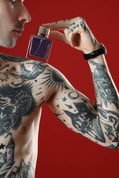 Tattooed young man with perfume on red background, closeup - Photo, image
