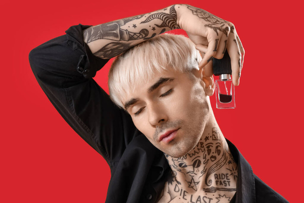 Tattooed young man with perfume on red background, closeup - Photo, Image