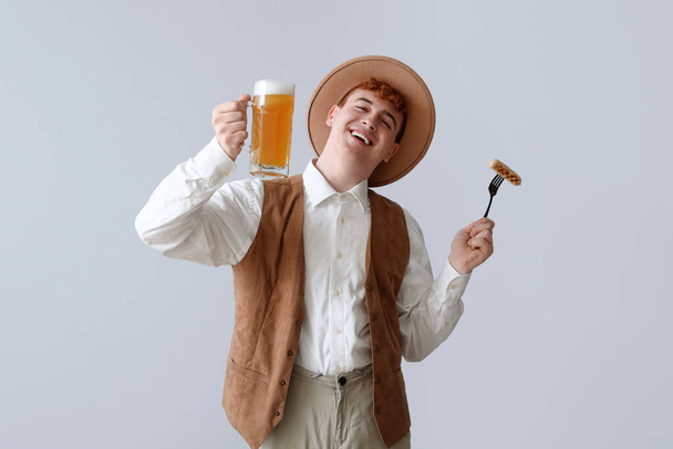 Young man in traditional German clothes with beer and sausage on light background - Photo, image