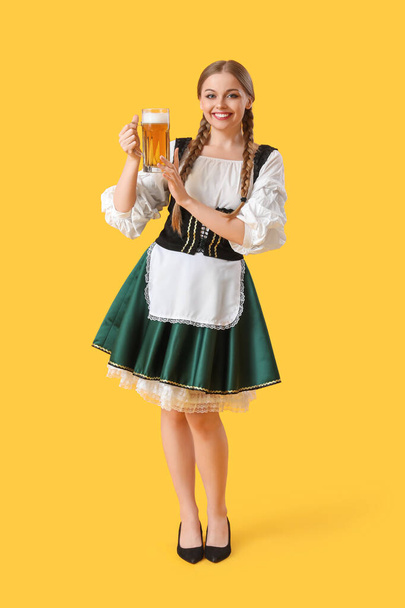 Beautiful Octoberfest waitress with beer on yellow background - Фото, зображення