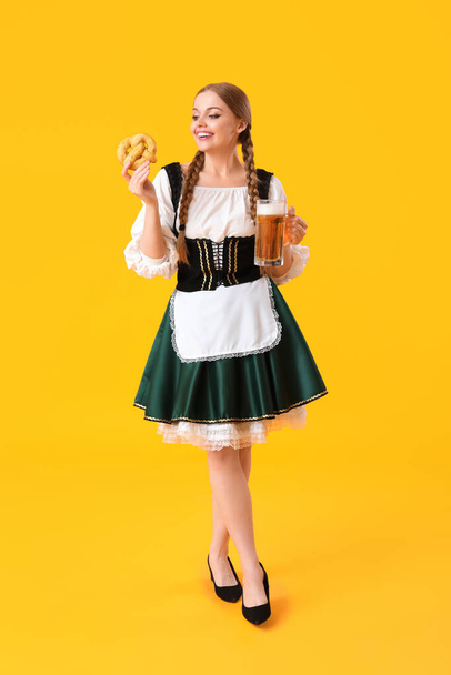 Schöne Oktoberfest-Kellnerin mit Bier und Brezel auf gelbem Hintergrund - Foto, Bild