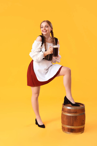 Beautiful Octoberfest waitress with beer and barrel on yellow background - Photo, Image