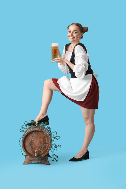 Beautiful Octoberfest waitress with beer and barrel on blue background - Foto, afbeelding