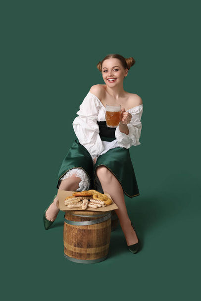 Beautiful Octoberfest waitress with beer and snacks sitting on green background - Photo, image