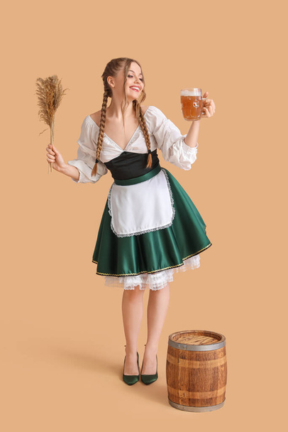 Beautiful Octoberfest waitress with beer and dry reeds on beige background - Photo, Image