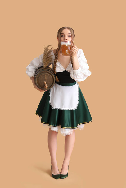 Beautiful Octoberfest waitress with beer and barrel on beige background - Fotoğraf, Görsel