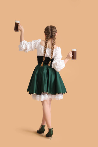 Piękna kelnerka Octoberfest z tańczącym piwem na beżowym tle, widok z tyłu - Zdjęcie, obraz